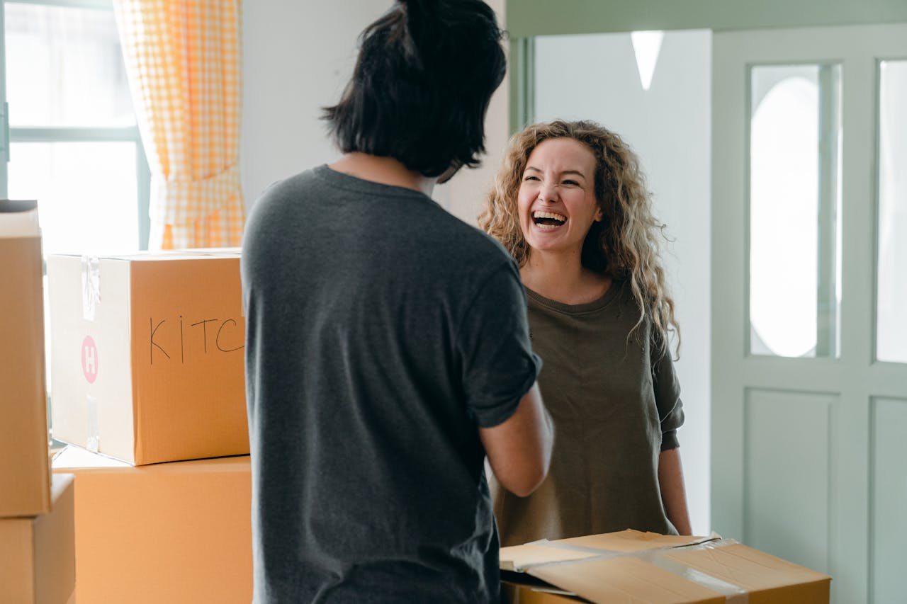 A joyful couple interacting with moving boxes in a bright living room, enjoying their new home.