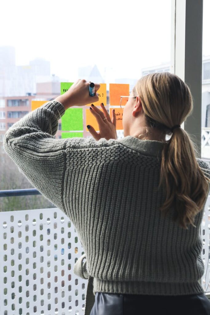 pexels photo 5839450 Woman writing on colorful sticky notes placed on a glass window indoors.
